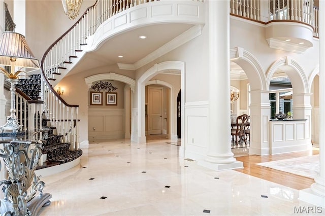 entrance foyer with a high ceiling, a decorative wall, arched walkways, crown molding, and ornate columns