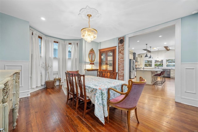 dining room with a chandelier, wainscoting, dark wood-style flooring, and a decorative wall