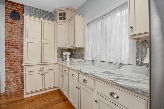 kitchen with cream cabinetry, light wood-style flooring, brick wall, and light stone countertops