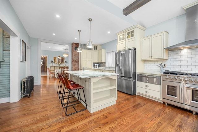 kitchen with appliances with stainless steel finishes, wall chimney range hood, a warming drawer, cream cabinets, and open shelves