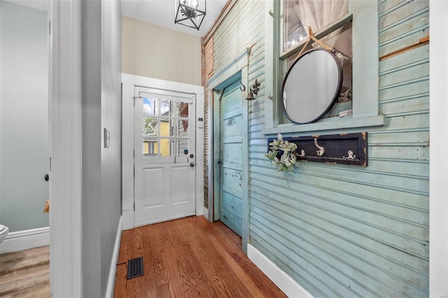 doorway featuring wood finished floors, baseboards, and wooden walls
