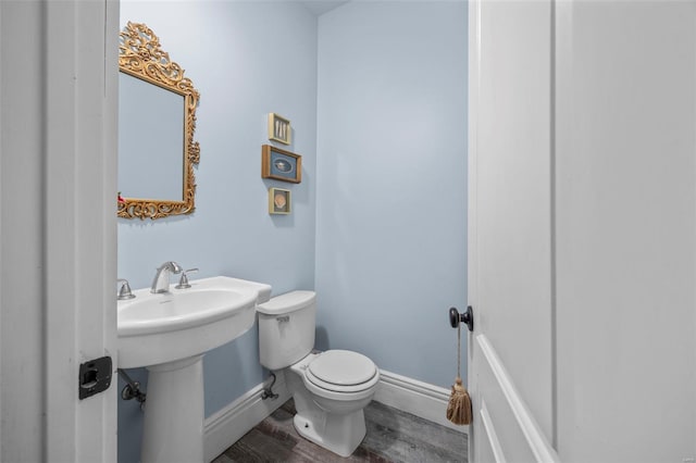 bathroom with toilet, wood finished floors, baseboards, and a sink