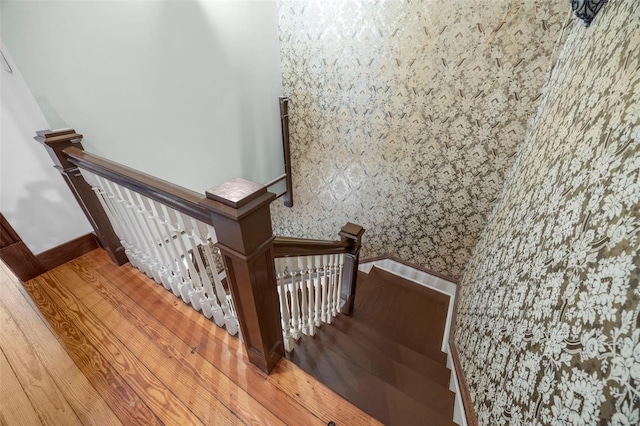 stairway with wallpapered walls and wood finished floors