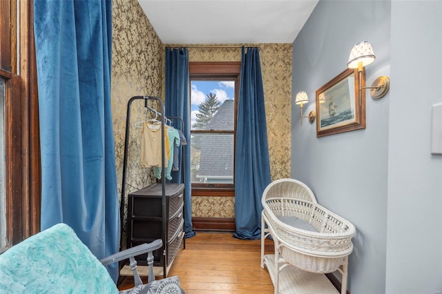 sitting room featuring wallpapered walls, wood-type flooring, and baseboards