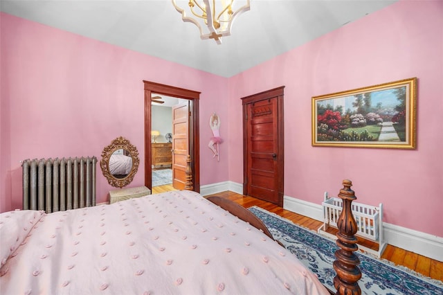 bedroom with radiator, a chandelier, baseboards, wood finished floors, and ensuite bath
