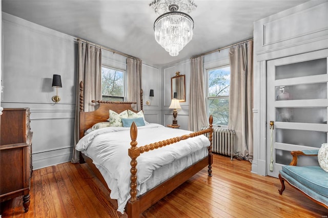 bedroom with radiator heating unit, multiple windows, hardwood / wood-style flooring, and a chandelier