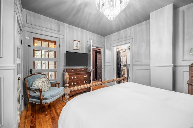 bedroom featuring wood finished floors, a chandelier, and a decorative wall
