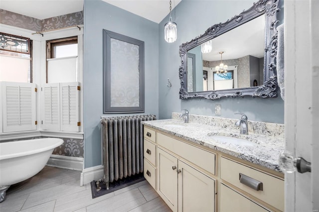 full bath featuring radiator heating unit, a chandelier, baseboards, a freestanding bath, and double vanity