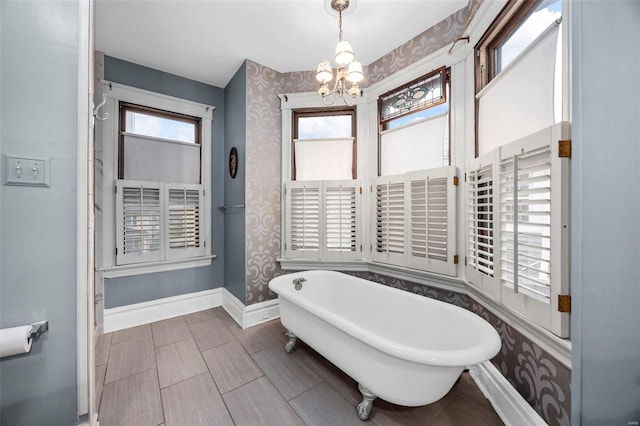 full bathroom featuring wallpapered walls, a chandelier, baseboards, and a soaking tub