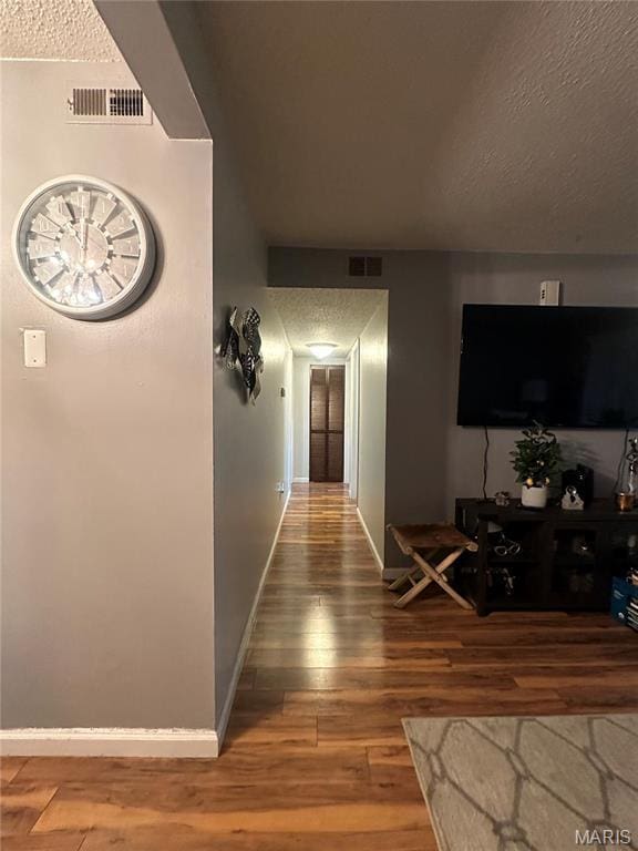 corridor featuring a textured ceiling, wood finished floors, and baseboards