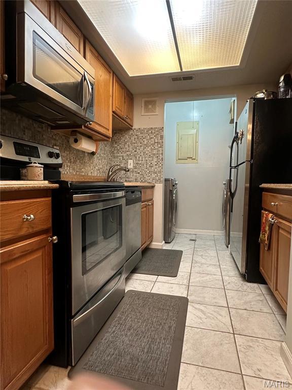 kitchen featuring appliances with stainless steel finishes, brown cabinetry, washing machine and clothes dryer, decorative backsplash, and a sink