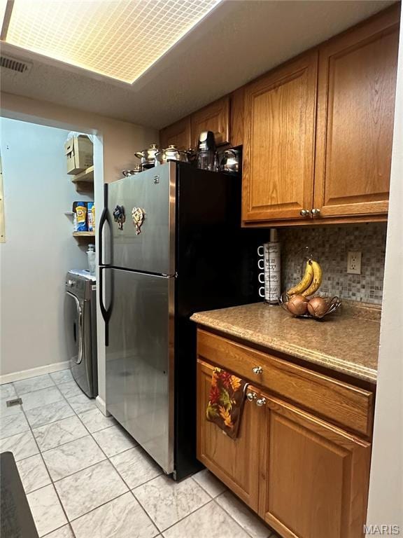 kitchen featuring freestanding refrigerator, brown cabinetry, decorative backsplash, light marble finish floors, and baseboards