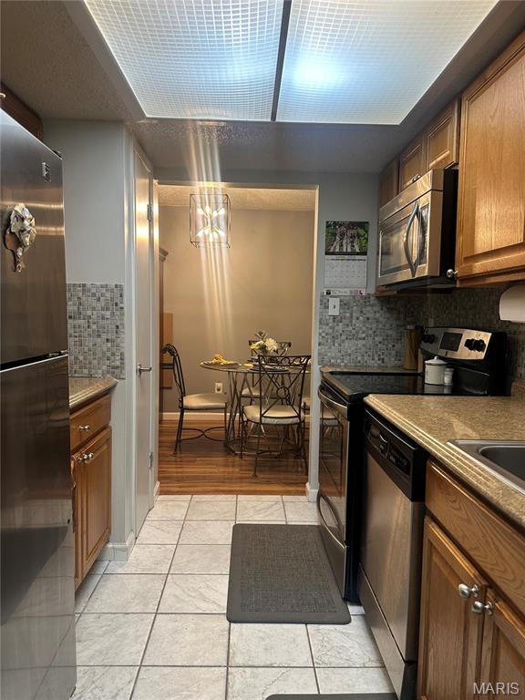 kitchen featuring appliances with stainless steel finishes, brown cabinets, tasteful backsplash, and light tile patterned floors