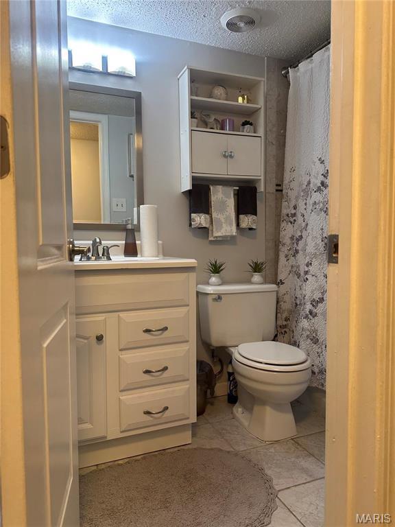 full bath featuring toilet, vanity, a textured ceiling, tile patterned flooring, and a shower with curtain
