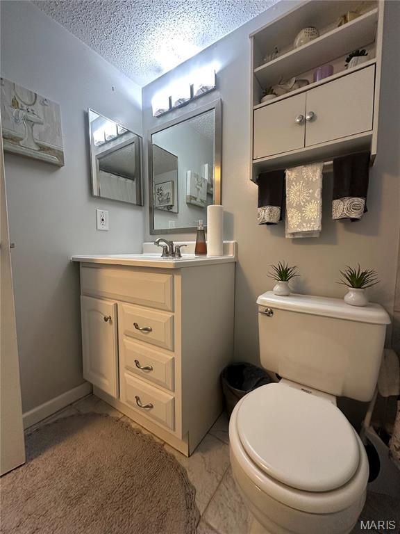 bathroom with a textured ceiling, marble look tile flooring, vanity, toilet, and baseboards