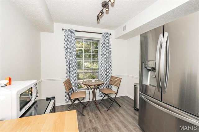 dining area featuring wood finished floors, a textured ceiling, track lighting, and baseboards