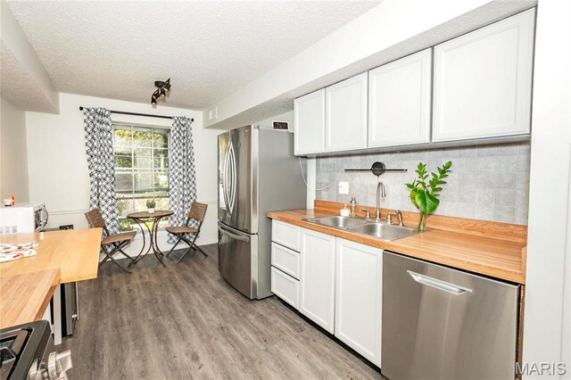kitchen with stainless steel appliances, butcher block countertops, a sink, white cabinets, and a textured ceiling