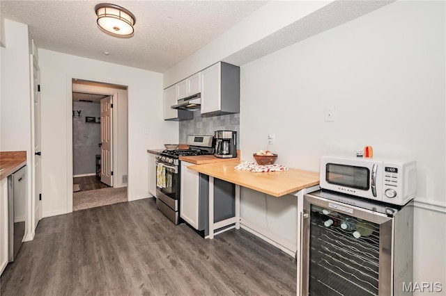 kitchen with stainless steel appliances, beverage cooler, dark wood-style floors, a textured ceiling, and under cabinet range hood