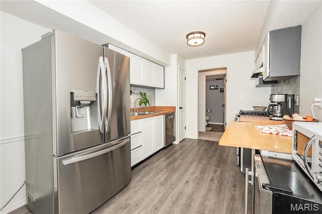 kitchen with appliances with stainless steel finishes, a sink, wood finished floors, under cabinet range hood, and white cabinetry