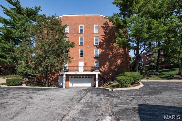 view of apartment building / complex featuring stairs, a garage, and asphalt driveway