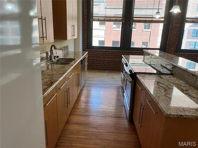 kitchen with appliances with stainless steel finishes, brick wall, a sink, hardwood / wood-style floors, and light stone countertops