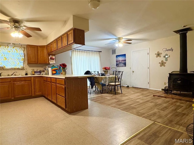 2101 Meadows Rd, Poplar Bluff, MO 63901 - kitchen with a ceiling fan, a peninsula, brown cabinetry, a wood stove, and light countertops