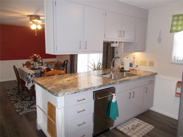 kitchen with a sink, dishwasher, a wainscoted wall, dark wood-style flooring, and white cabinetry