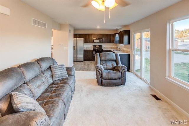 living area featuring a ceiling fan, plenty of natural light, baseboards, and light carpet