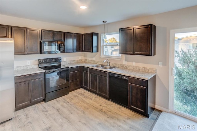 kitchen with black appliances, a sink, dark brown cabinets, light countertops, and light wood-style floors