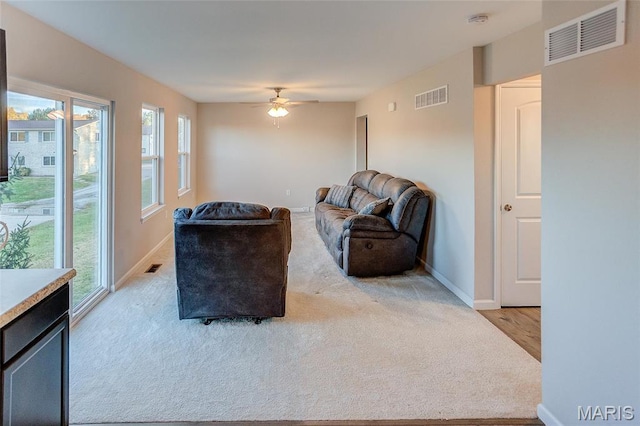 carpeted living area with plenty of natural light, baseboards, ceiling fan, and wood finished floors