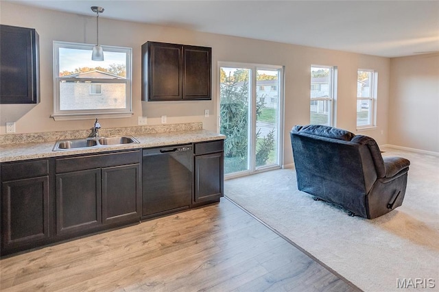 kitchen with black dishwasher, a sink, light countertops, open floor plan, and light wood-style floors