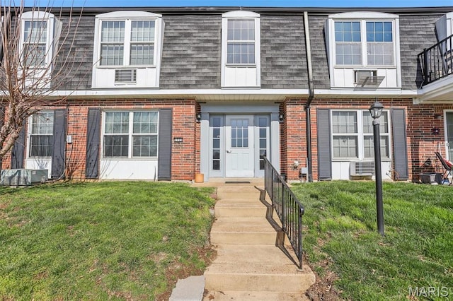 multi unit property with brick siding, mansard roof, roof with shingles, and a front lawn