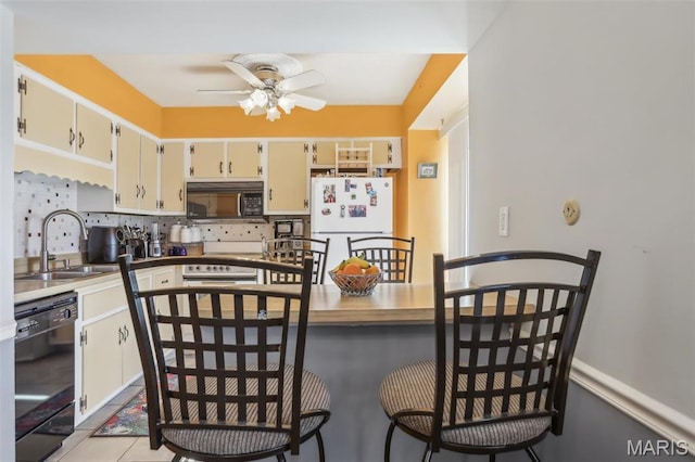 kitchen with black appliances, ceiling fan, a sink, and a breakfast bar area