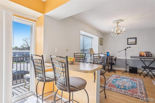 dining space with light wood-style floors, a chandelier, baseboards, and a textured ceiling