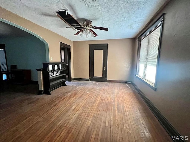 4873 Kossuth Ave, Saint Louis, MO 63115 - unfurnished living room with hardwood / wood-style floors, baseboards, a textured ceiling, ceiling fan, and arched walkways