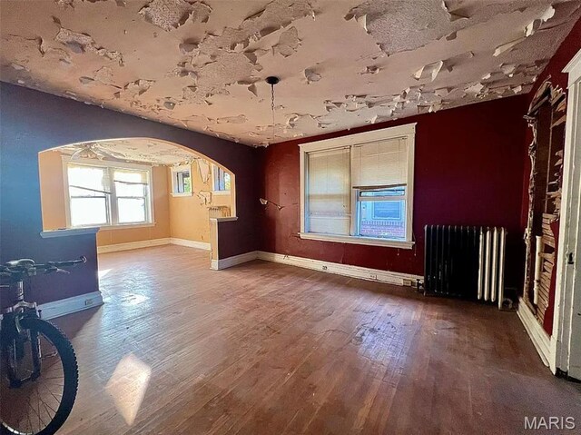4873 Kossuth Ave, Saint Louis, MO 63115 - empty room featuring radiator heating unit, arched walkways, wood finished floors, and baseboards