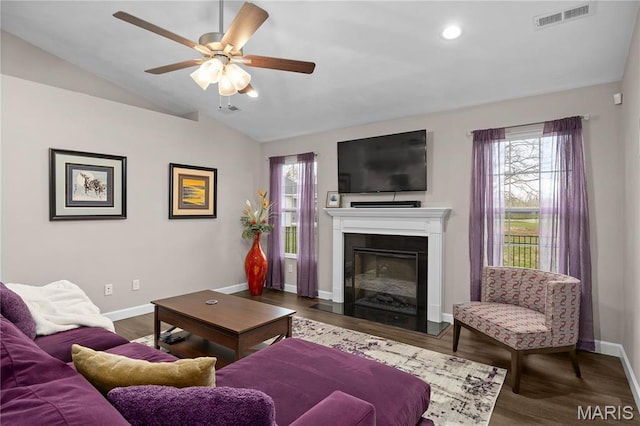 living area featuring ceiling fan, baseboards, lofted ceiling, wood finished floors, and a fireplace with flush hearth
