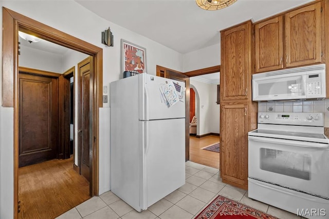 3981 Canterbury Dr, Saint Louis, MO 63121 - kitchen featuring white appliances, arched walkways, light tile patterned floors, brown cabinets, and decorative backsplash