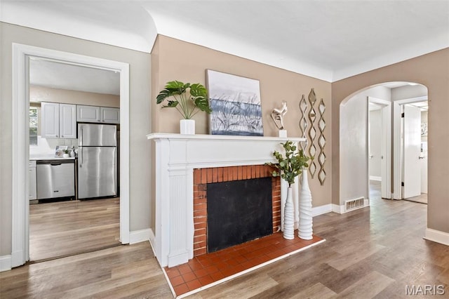 309 N Schlueter Ave, Saint Louis, MO 63135 - unfurnished living room with arched walkways, light wood finished floors, and a brick fireplace