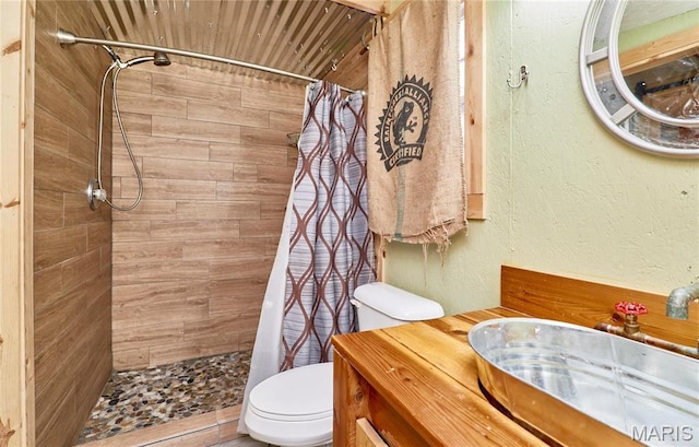 full bath featuring toilet, a tile shower, vanity, and a textured wall