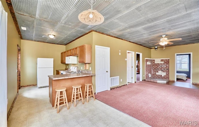 kitchen featuring white appliances, a peninsula, light countertops, ceiling fan, and a kitchen bar