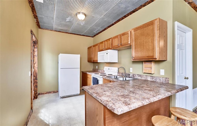 kitchen featuring white appliances, baseboards, a sink, a peninsula, and a kitchen breakfast bar