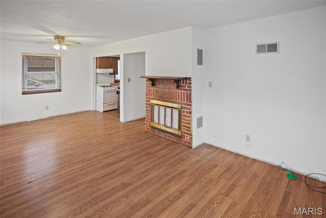 unfurnished living room featuring ceiling fan, light wood-style floors, and a brick fireplace