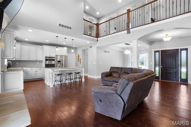 9336 Excelsior Rd, Gerald, MO 63037 - living room featuring arched walkways, dark wood finished floors, decorative columns, baseboards, and a towering ceiling