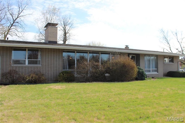 rear view of property with a chimney, a lawn, and brick siding