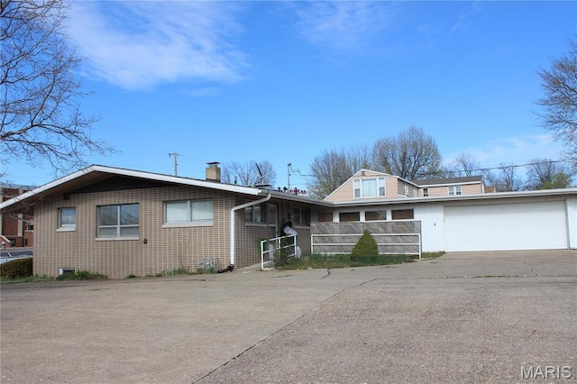 view of front of property featuring driveway, a chimney, brick siding, and fence