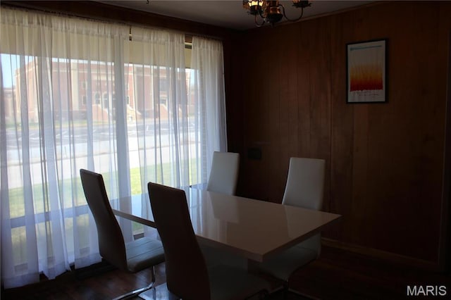 dining area featuring plenty of natural light, a chandelier, wooden walls, and wood finished floors