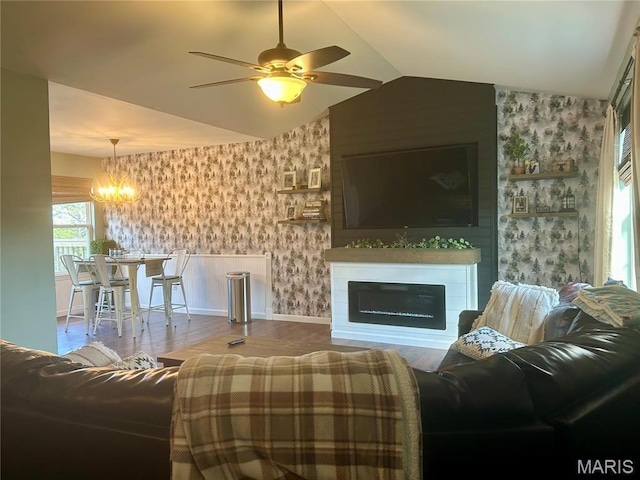 living area featuring wallpapered walls, a chandelier, baseboards, lofted ceiling, and a ceiling fan