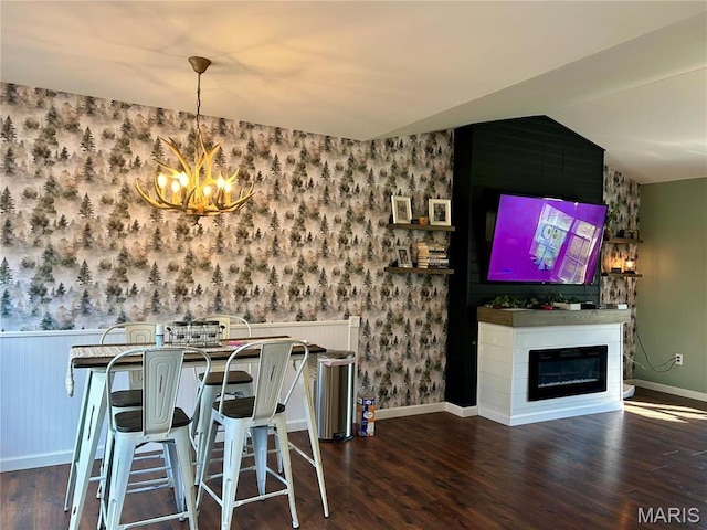 unfurnished dining area with wallpapered walls, a chandelier, dark wood-style flooring, a fireplace, and wainscoting