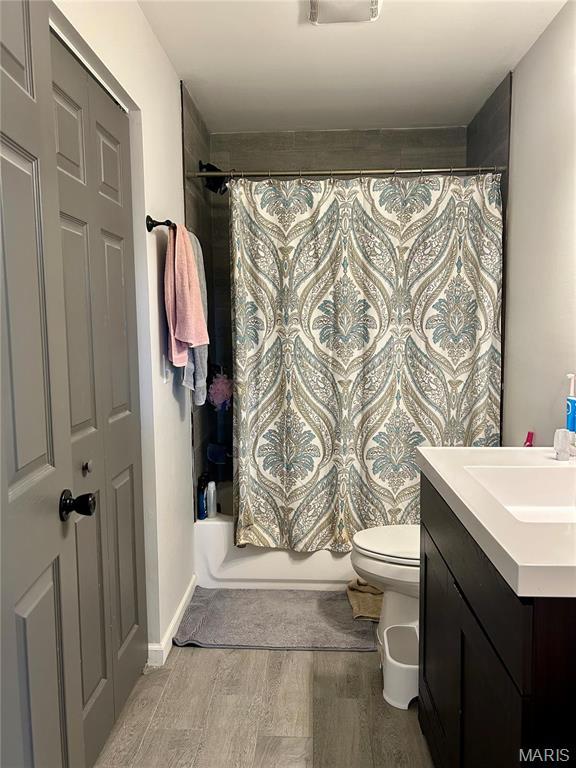 bathroom featuring wood finished floors, shower / bathtub combination with curtain, vanity, and toilet